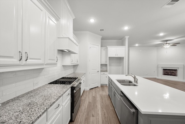 kitchen with appliances with stainless steel finishes, sink, light hardwood / wood-style floors, white cabinetry, and an island with sink