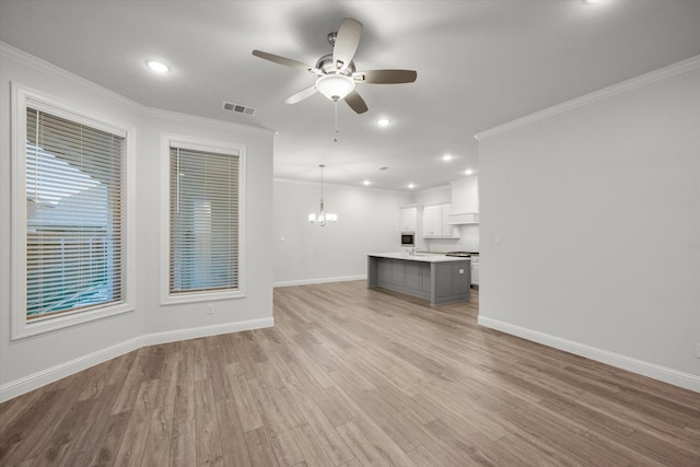 unfurnished living room featuring ornamental molding, ceiling fan with notable chandelier, and light wood-type flooring