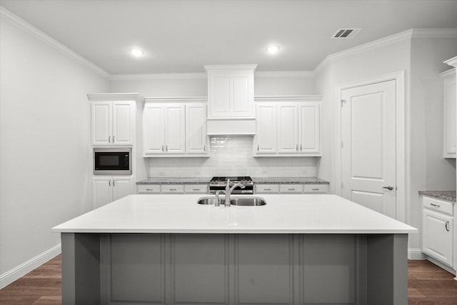 kitchen featuring built in microwave, an island with sink, sink, white cabinets, and dark wood-type flooring