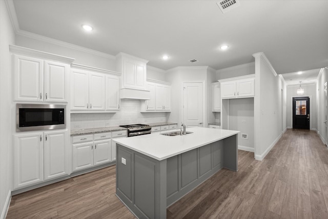 kitchen featuring light wood-type flooring, stainless steel appliances, a kitchen island with sink, sink, and white cabinetry