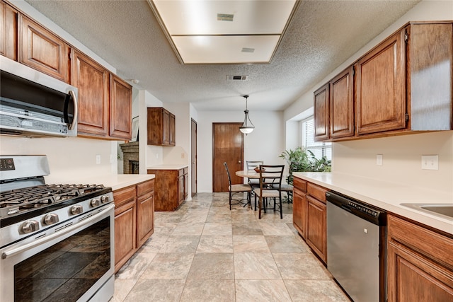 kitchen featuring a textured ceiling, stainless steel appliances, and hanging light fixtures