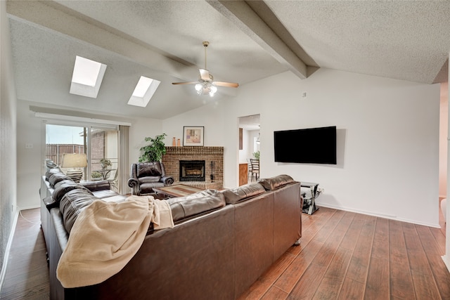 living room with ceiling fan, a brick fireplace, lofted ceiling with beams, dark hardwood / wood-style floors, and a textured ceiling