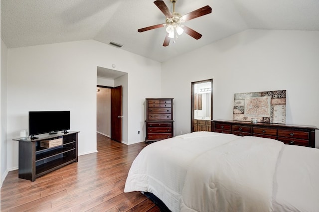 bedroom with hardwood / wood-style floors, lofted ceiling, ceiling fan, a textured ceiling, and connected bathroom