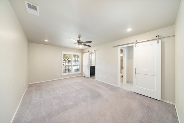 unfurnished living room featuring light carpet, a barn door, and ceiling fan