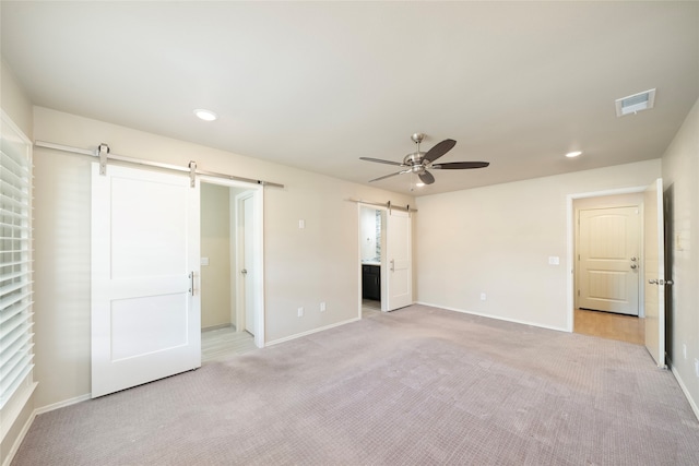 unfurnished bedroom with ensuite bath, a barn door, light colored carpet, and ceiling fan