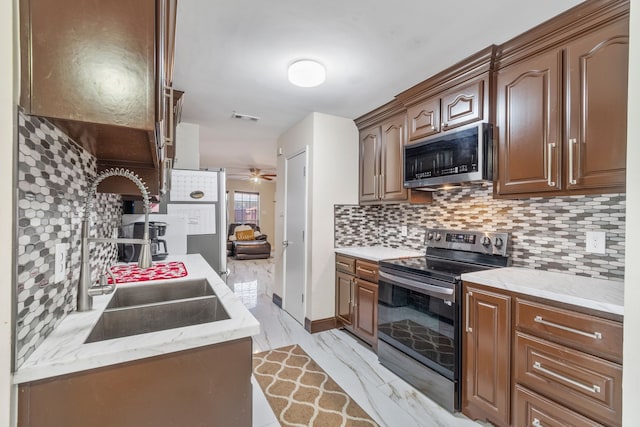 kitchen with light stone countertops, appliances with stainless steel finishes, sink, backsplash, and ceiling fan