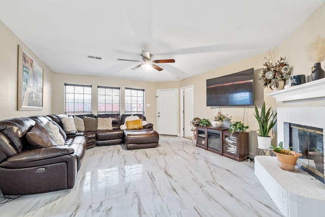 living room with a tile fireplace and ceiling fan