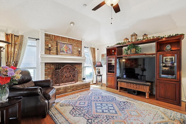 living room with a fireplace, a textured ceiling, vaulted ceiling, ceiling fan, and light hardwood / wood-style flooring