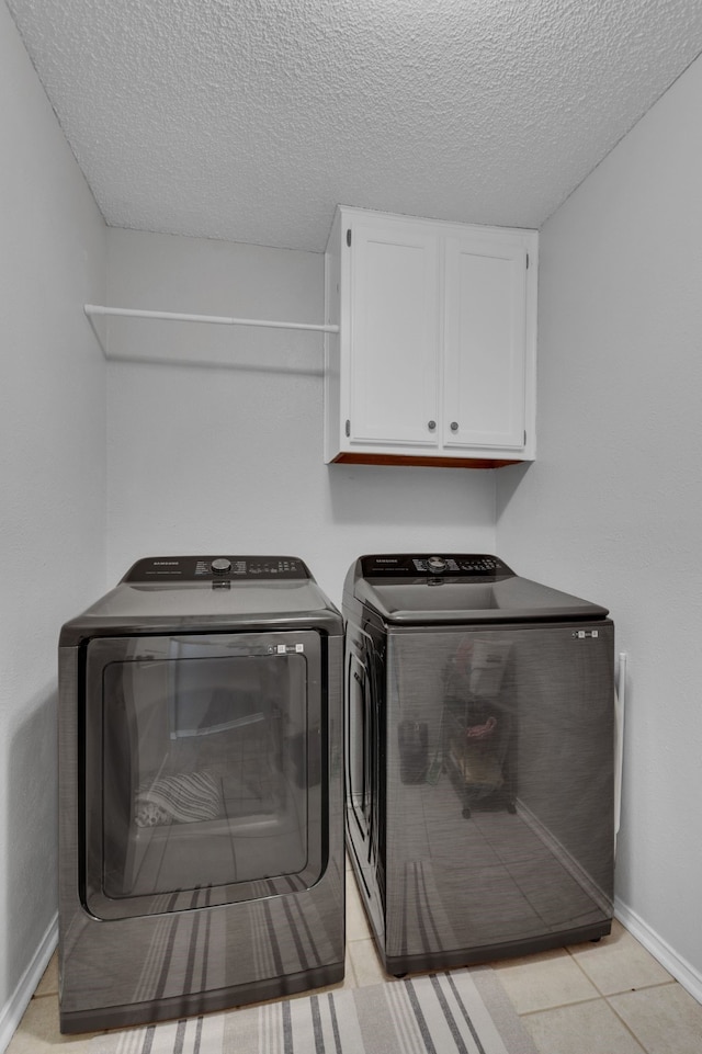 laundry area featuring light tile patterned floors, a textured ceiling, cabinets, and separate washer and dryer