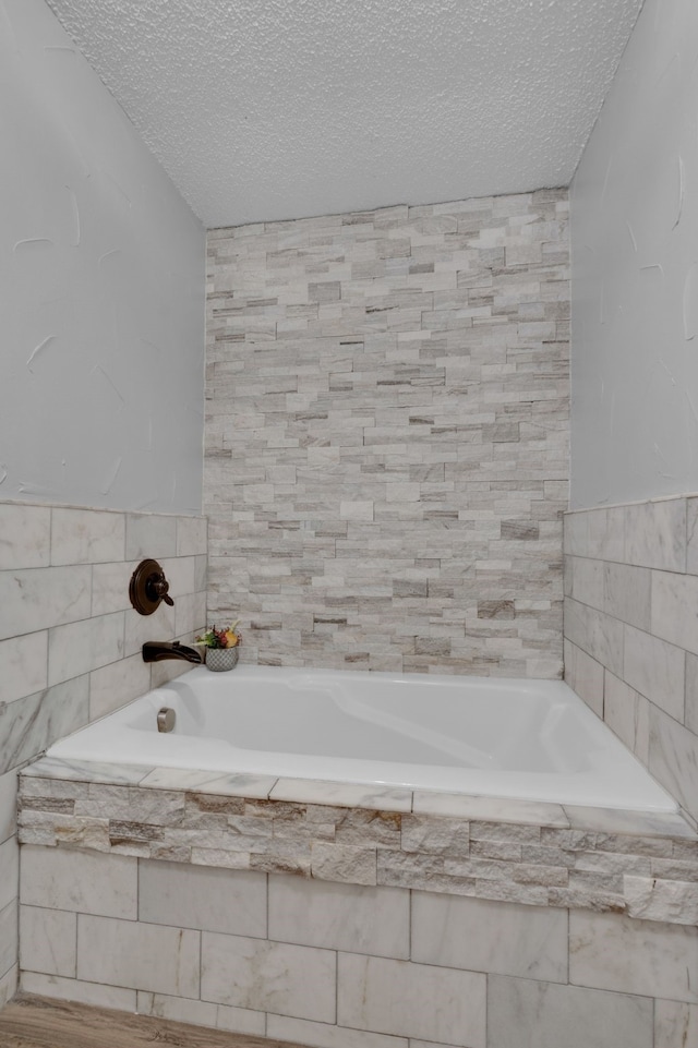 bathroom with tile walls, a textured ceiling, and tiled bath