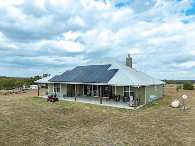 rear view of property featuring a patio area, a lawn, and solar panels