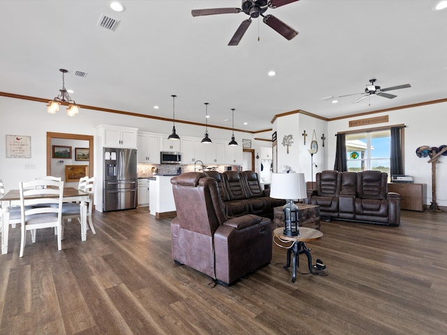 living room featuring dark wood-type flooring, crown molding, and ceiling fan with notable chandelier