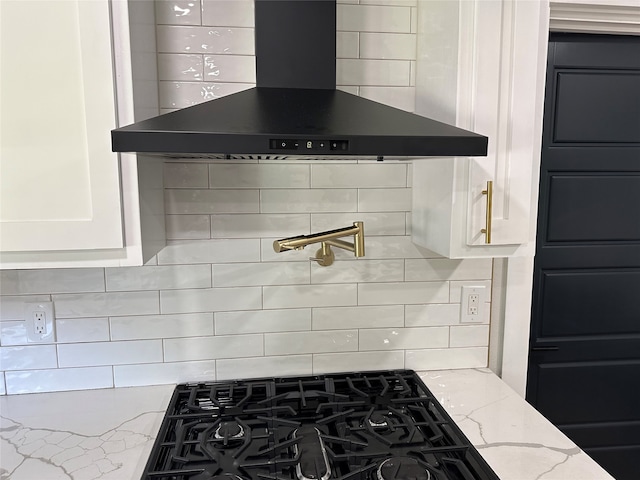 kitchen featuring tasteful backsplash, white cabinetry, stovetop, light stone countertops, and wall chimney range hood