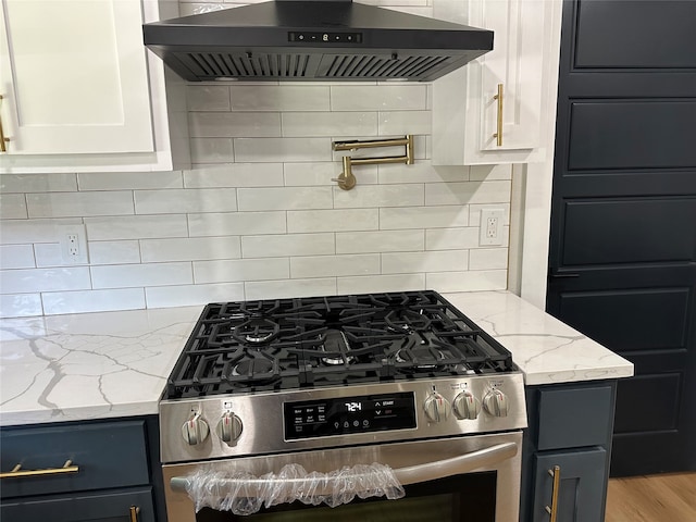 kitchen with extractor fan, stainless steel gas range oven, light stone counters, white cabinets, and backsplash