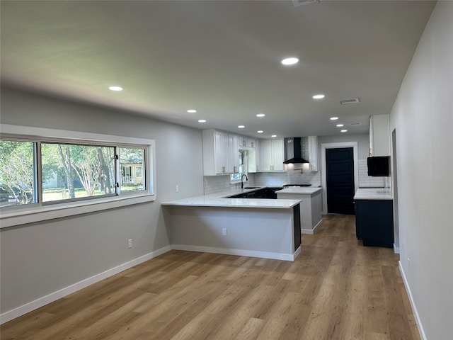 kitchen featuring white cabinetry, tasteful backsplash, kitchen peninsula, wall chimney exhaust hood, and light wood-type flooring