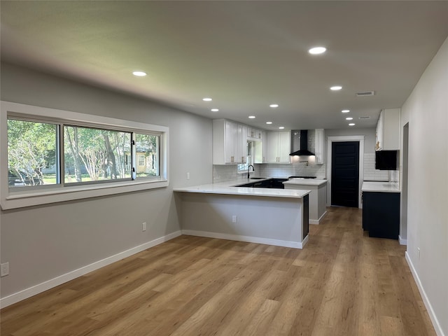 kitchen featuring sink, white cabinets, decorative backsplash, kitchen peninsula, and wall chimney exhaust hood