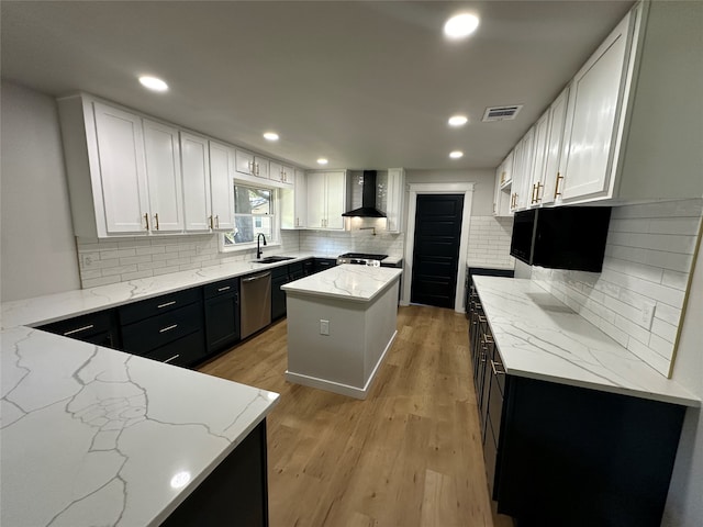 kitchen with white cabinetry, wall chimney range hood, light stone counters, and a center island