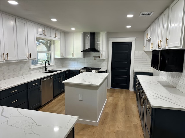 kitchen with appliances with stainless steel finishes, a kitchen island, sink, white cabinets, and wall chimney exhaust hood