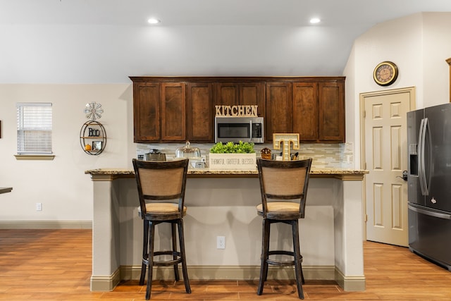 kitchen with light hardwood / wood-style floors, stainless steel appliances, light stone countertops, and vaulted ceiling