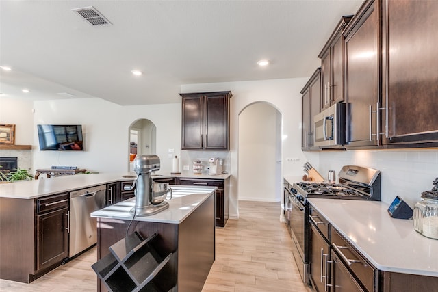 kitchen featuring a kitchen island, decorative backsplash, stainless steel appliances, dark brown cabinetry, and light wood-type flooring