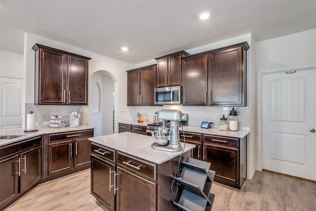 kitchen with dark brown cabinetry, stainless steel appliances, tasteful backsplash, and light wood-type flooring