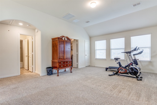 exercise room with vaulted ceiling and light colored carpet