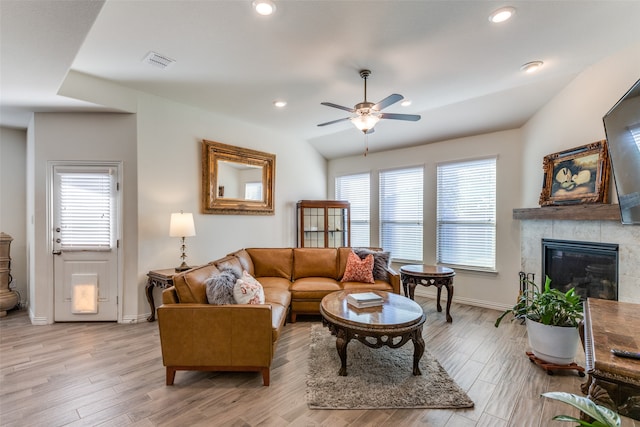 living room featuring a tiled fireplace, light hardwood / wood-style floors, lofted ceiling, and ceiling fan