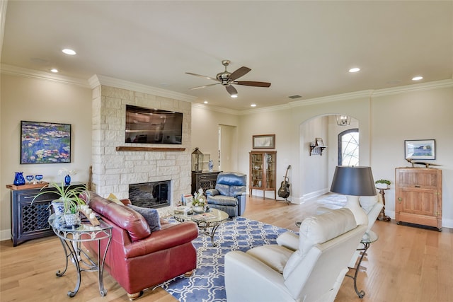 living room with crown molding, a fireplace, light wood-type flooring, and ceiling fan