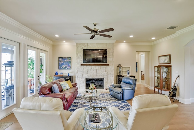 living room with light wood-type flooring, french doors, a stone fireplace, ceiling fan, and ornamental molding