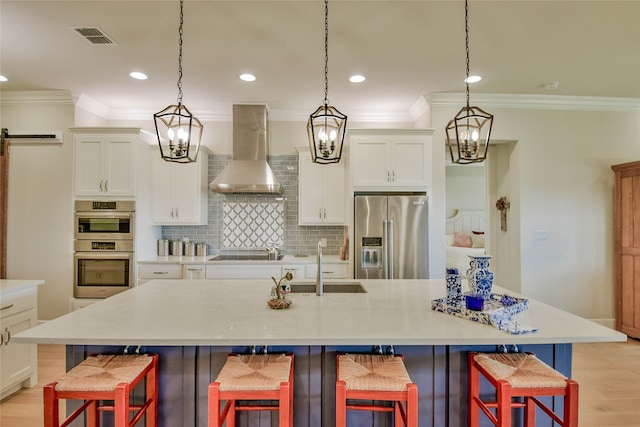 kitchen with wall chimney exhaust hood, a spacious island, appliances with stainless steel finishes, and a kitchen bar