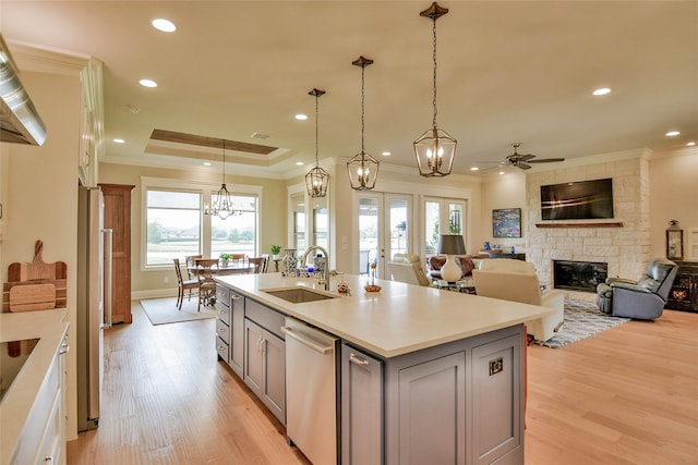 kitchen featuring appliances with stainless steel finishes, sink, a stone fireplace, light hardwood / wood-style floors, and a kitchen island with sink