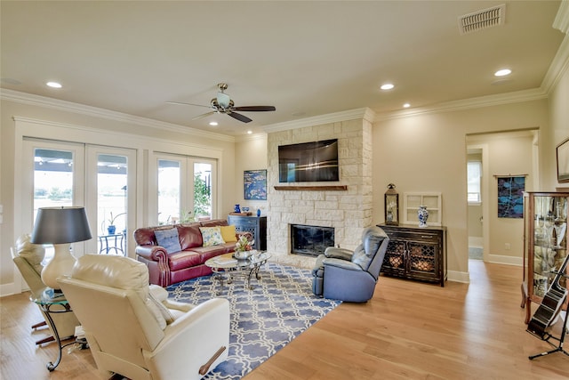 living room featuring ornamental molding, light hardwood / wood-style flooring, and a stone fireplace