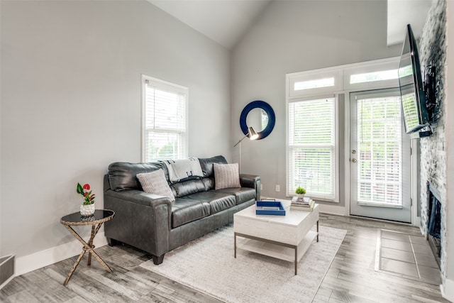 living room featuring high vaulted ceiling, a fireplace, light wood-type flooring, and a healthy amount of sunlight