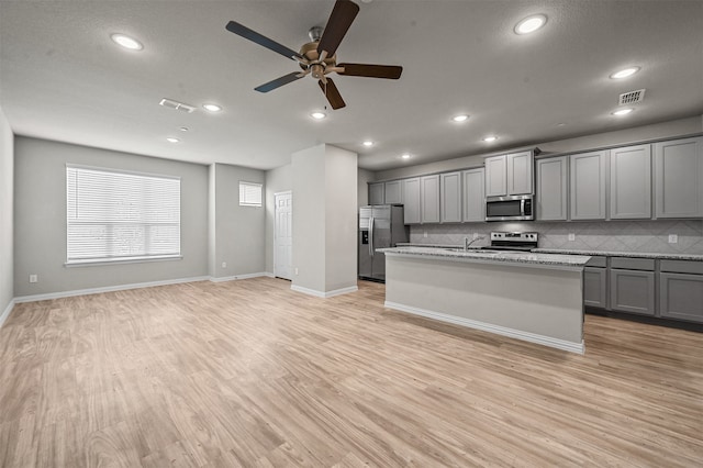 kitchen with an island with sink, gray cabinetry, stainless steel appliances, and light hardwood / wood-style floors