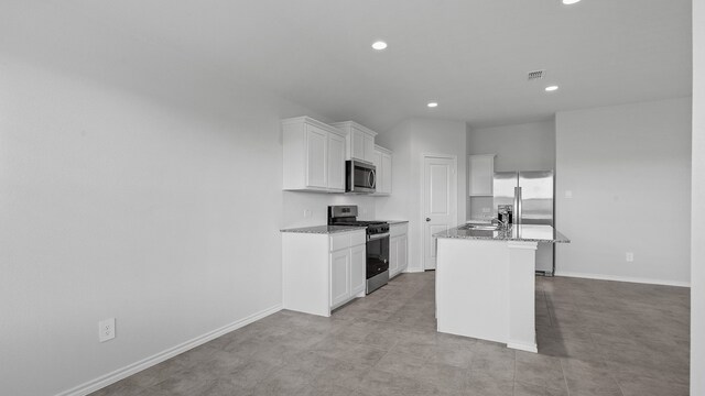 kitchen with stainless steel appliances, a center island with sink, sink, white cabinets, and light stone counters