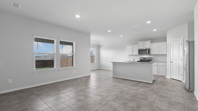 kitchen with light stone counters, appliances with stainless steel finishes, white cabinetry, a kitchen island with sink, and sink