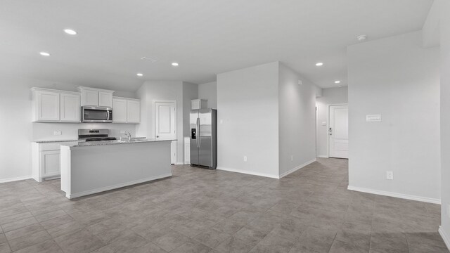 kitchen featuring a kitchen island with sink, stainless steel appliances, sink, light stone countertops, and white cabinetry