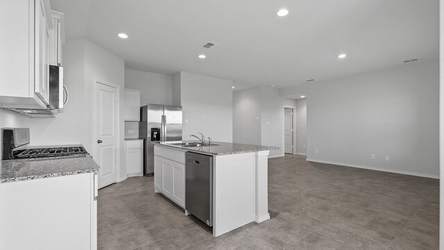 kitchen featuring light stone counters, stainless steel appliances, a center island with sink, and white cabinets