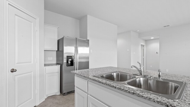 kitchen with white cabinetry, stainless steel refrigerator with ice dispenser, light stone counters, and sink