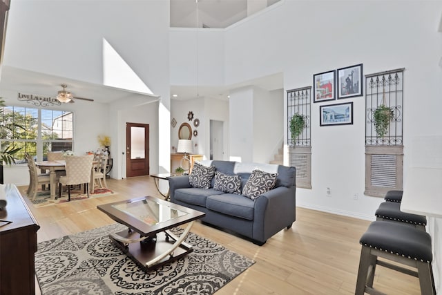 living room featuring a high ceiling, ceiling fan, and light hardwood / wood-style flooring