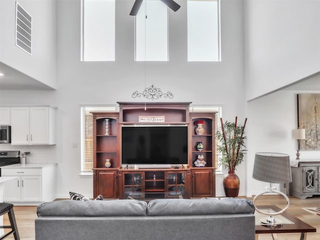 living room with light wood-style flooring, a high ceiling, a ceiling fan, and visible vents
