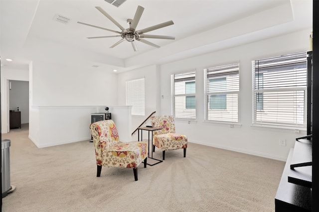 living area with ceiling fan, light colored carpet, plenty of natural light, and a raised ceiling