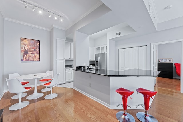 kitchen with light wood-type flooring, a center island, stainless steel fridge, white cabinets, and ornamental molding