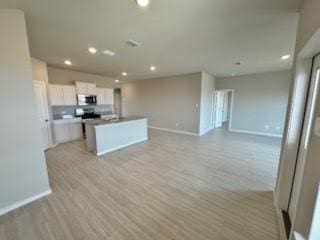 kitchen with white cabinetry, a center island with sink, and light hardwood / wood-style floors