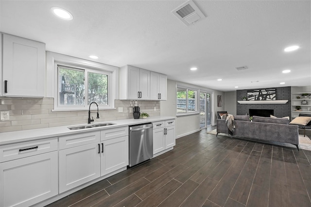 kitchen with white cabinetry, stainless steel dishwasher, sink, and a fireplace