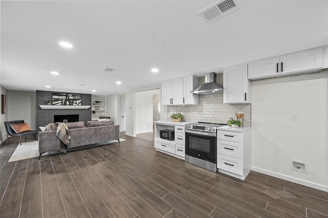 kitchen featuring wall chimney range hood, white cabinets, a brick fireplace, dark hardwood / wood-style floors, and electric stove