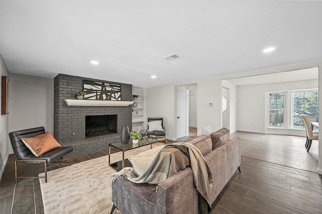 living room with dark hardwood / wood-style floors, built in shelves, and a brick fireplace