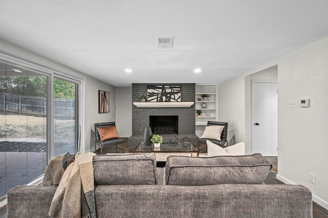 living room with built in features, wood-type flooring, a textured ceiling, and a fireplace