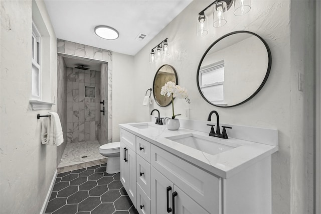 bathroom featuring vanity, a tile shower, toilet, and tile patterned flooring