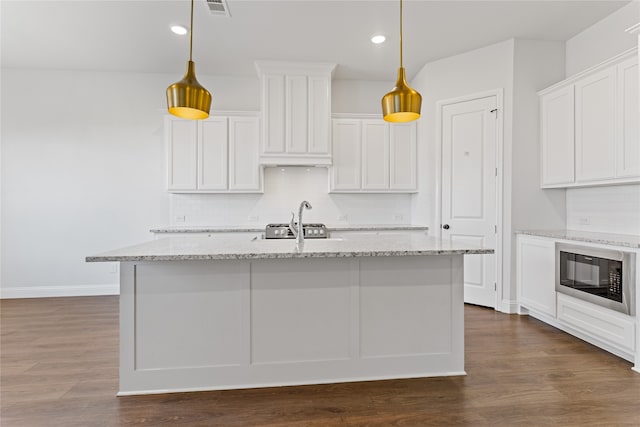 kitchen with light stone countertops, white cabinets, dark hardwood / wood-style floors, hanging light fixtures, and an island with sink